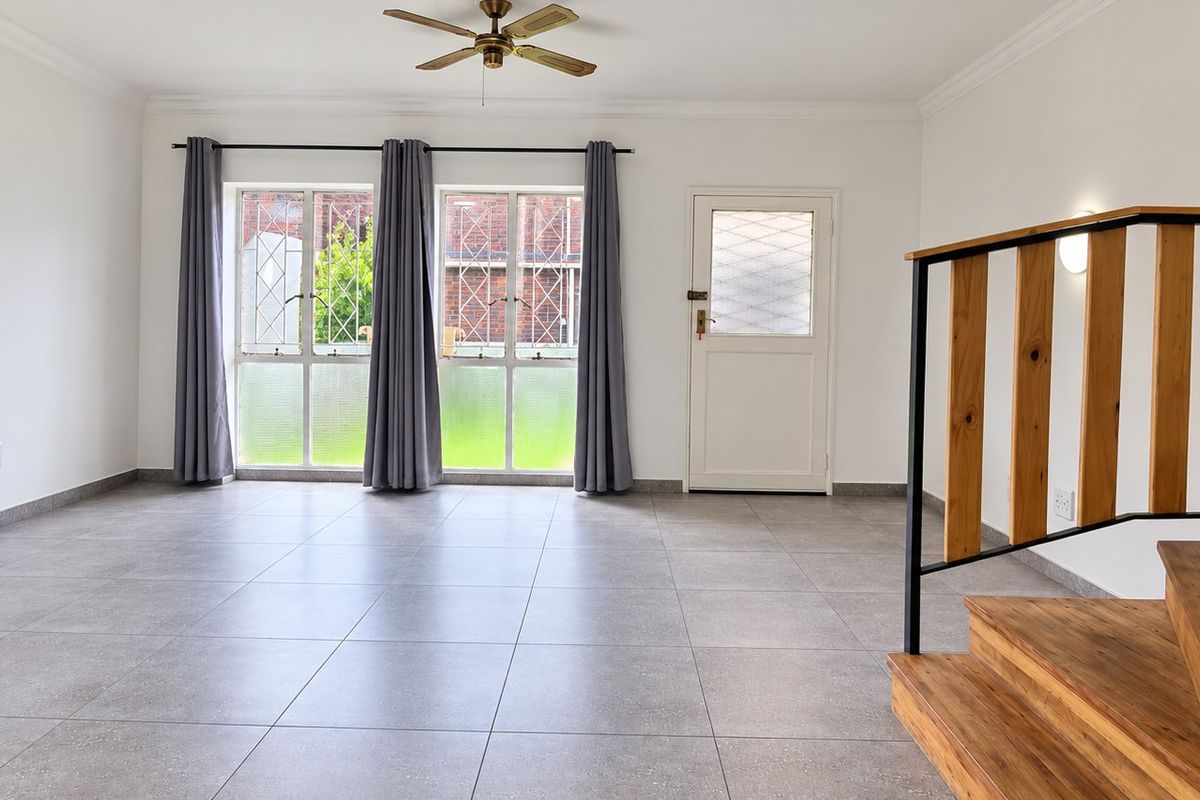 Spacious open-plan living area featuring neutral tiled flooring, a wooden staircase with metal balustrade, and direct access to the exterior.