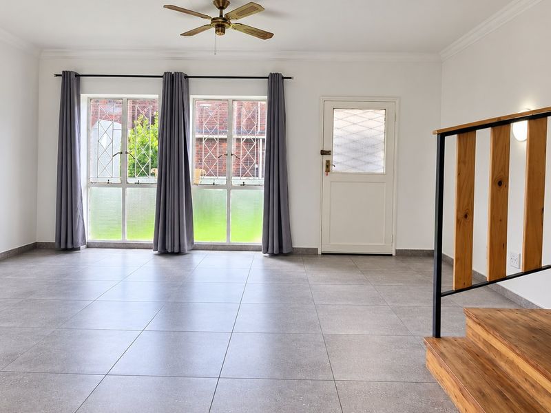 Spacious open-plan living area featuring neutral tiled flooring, a wooden staircase with metal balustrade, and direct access to the exterior.