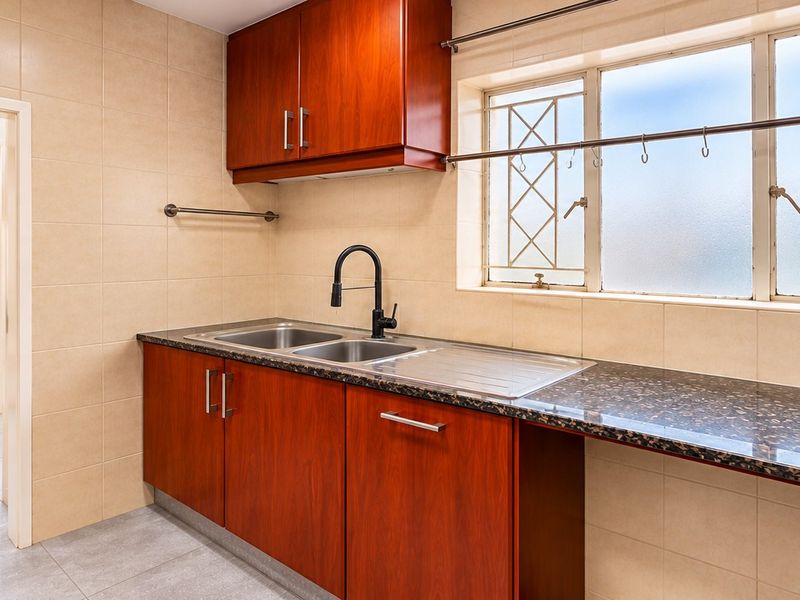 A functional scullery featuring built-in wooden cabinetry, granite countertops, a double sink, and tiled finishes, providing a practical secondary workspace.