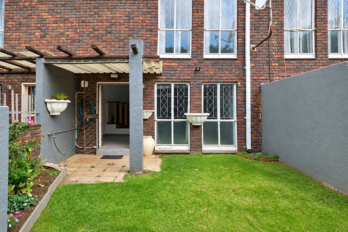 Rear exterior view of a townhouse featuring a brick facade, a small paved patio area with a pergola, and a private lawn.