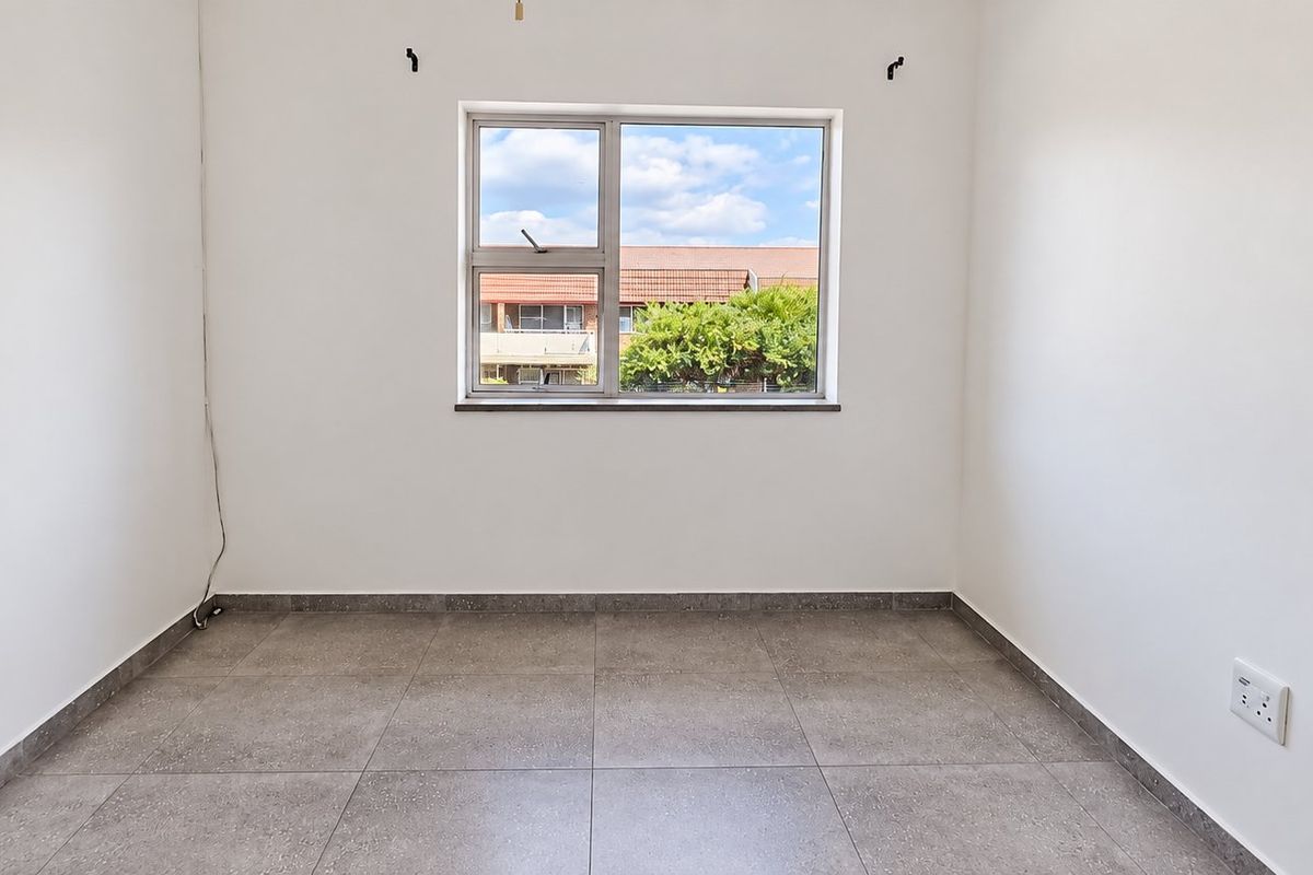 A bright, empty bedroom featuring neutral tiled flooring and a large window, providing a clean and versatile space ready for personalization.