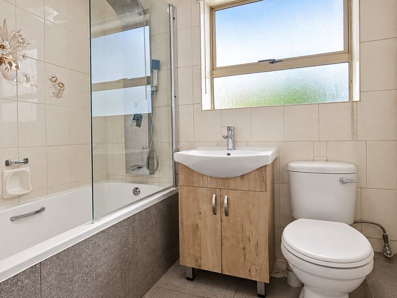 A functional bathroom featuring a bathtub with a glass screen, a vanity unit with a washbasin, and a standard toilet with tiled finishes.