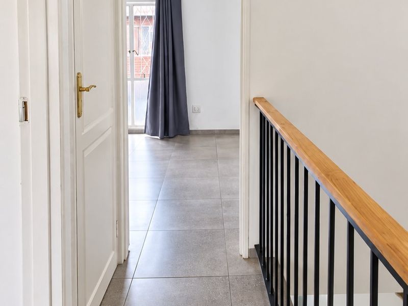 A bright, clean upstairs hallway featuring modern grey floor tiles, a sleek metal balustrade with a wooden handrail, and built-in storage cabinetry.