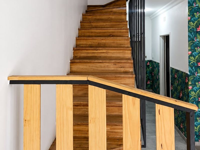 A bright hallway featuring a timber staircase with a modern metal and wood balustrade, complemented by tiled flooring and decorative wallpaper.