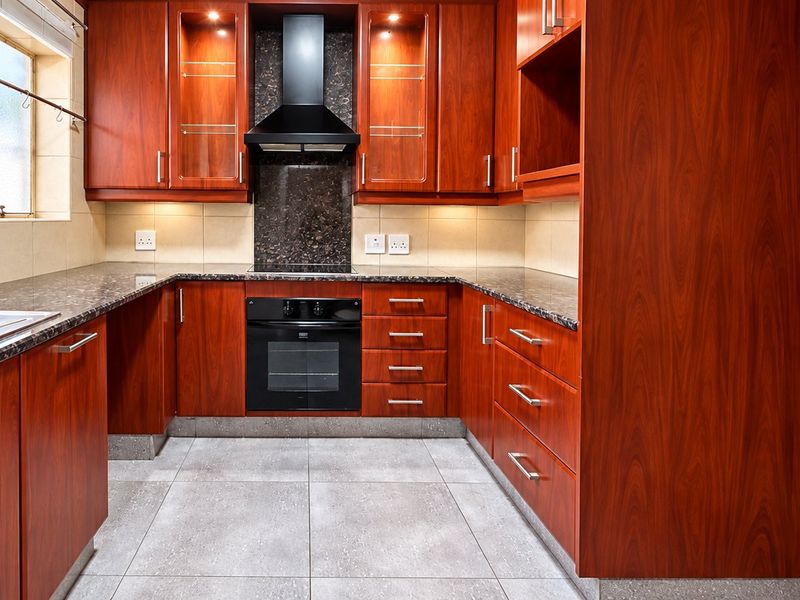 A well-maintained kitchen featuring rich wood-toned cabinetry, granite countertops, integrated oven, extractor fan, and neutral tiled flooring with ample storage space.