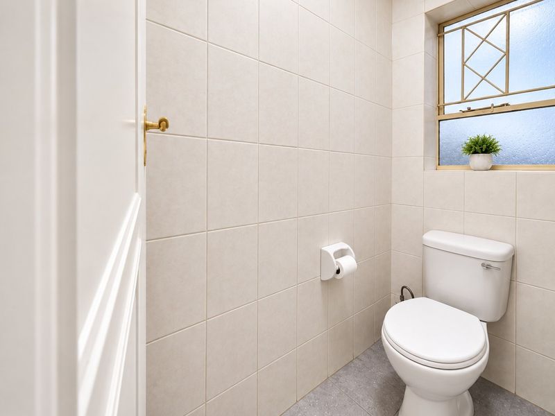 A clean and functional guest bathroom featuring neutral wall tiles, tiled flooring, and a window with security bars.