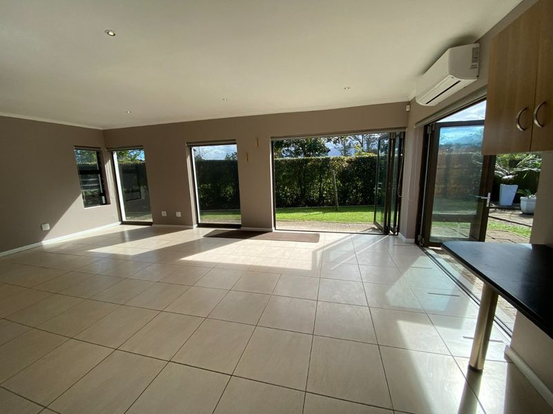 Spacious open-plan living area featuring large bi-fold doors opening to the garden, tiled flooring, and a wall-mounted air conditioning unit.