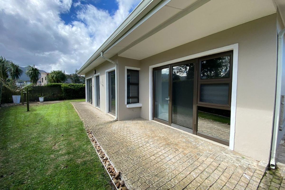 Rear view of the property featuring a paved patio area, sliding glass doors, and a well-maintained lawn.