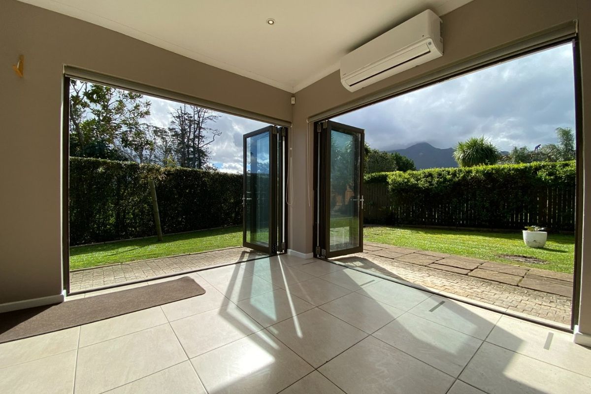 Bright and spacious living area featuring large bi-fold doors opening to a private garden, tiled flooring, and a wall-mounted air conditioning unit.