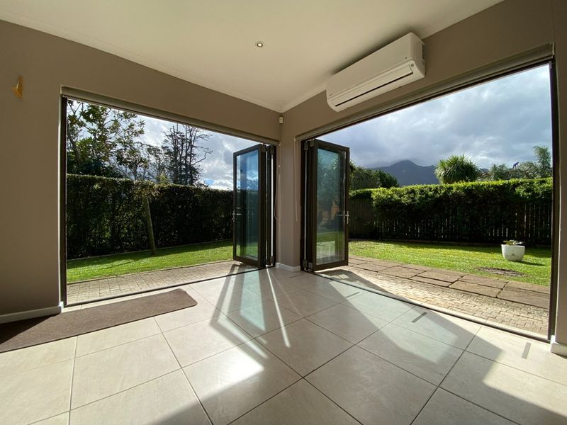 Bright and spacious living area featuring large bi-fold doors opening to a private garden, tiled flooring, and a wall-mounted air conditioning unit.