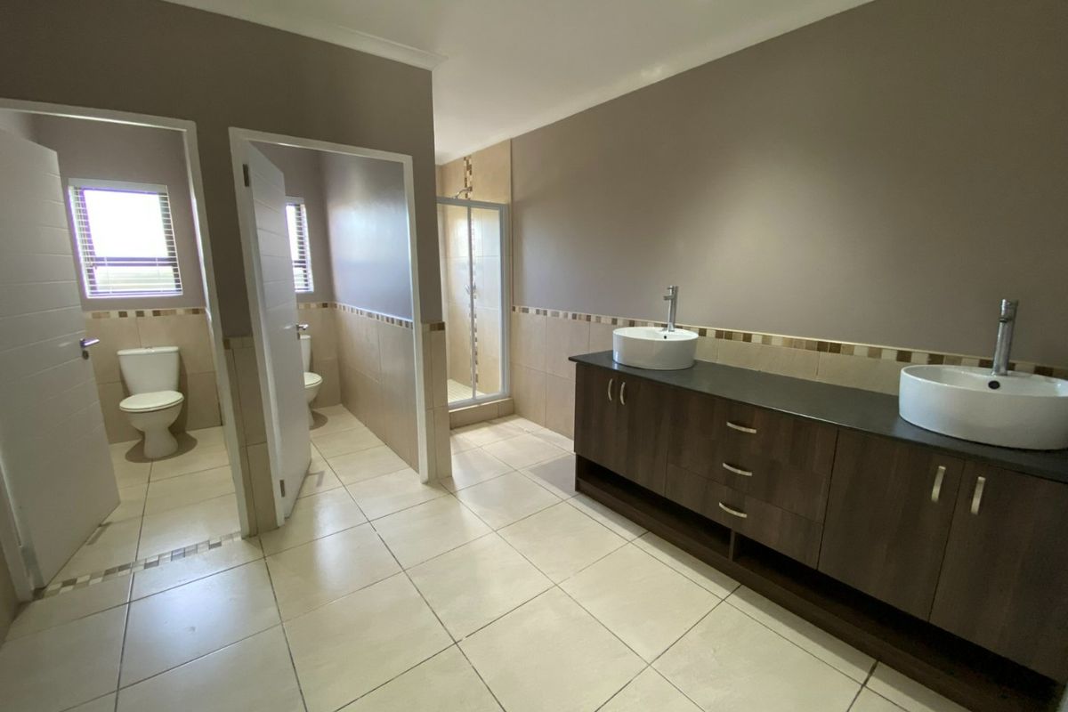 Spacious bathroom featuring a double vanity with vessel sinks, a separate shower enclosure, and a private toilet area with neutral tiled finishes.