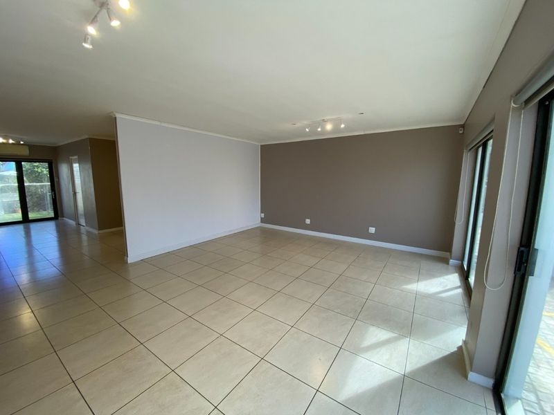 A spacious, empty living area featuring neutral-toned walls, large format floor tiles, and sliding glass doors that provide ample natural light.
