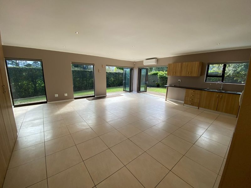 Spacious open-plan living area featuring tiled floors, built-in kitchen cabinetry, and multiple folding glass doors providing seamless access to the garden.