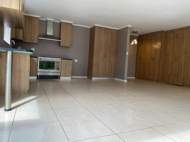 Spacious open-plan kitchen and living area featuring modern wood-finish cabinetry, tiled flooring, and integrated lighting throughout.