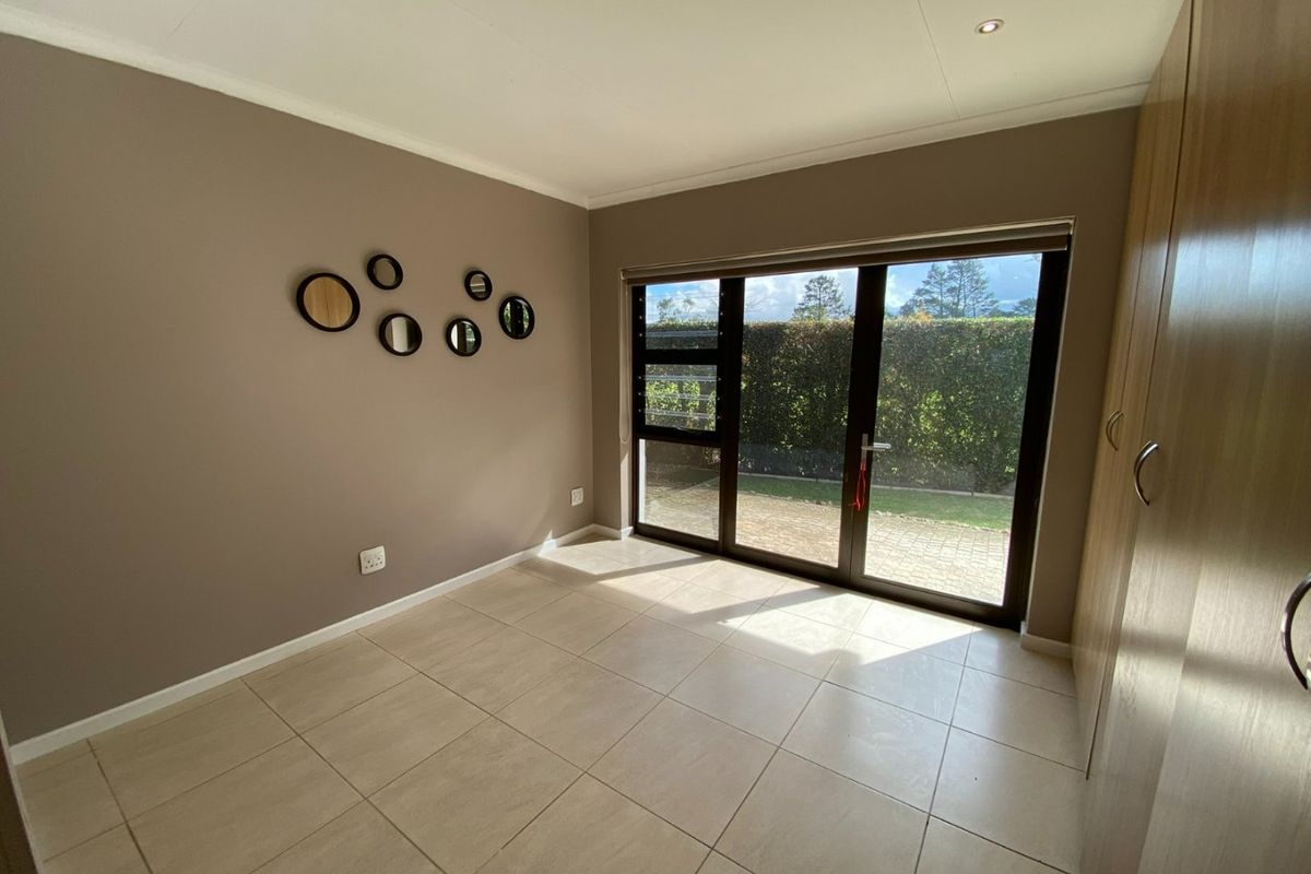 A bright, empty bedroom featuring tiled flooring, built-in cupboards, and a large sliding glass door providing direct access to the garden.