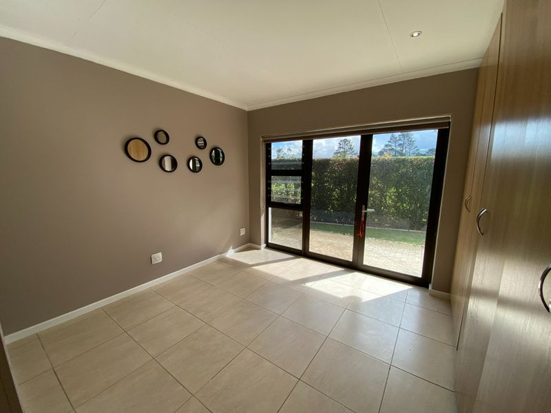 A bright, empty bedroom featuring tiled flooring, built-in cupboards, and a large sliding glass door providing direct access to the garden.