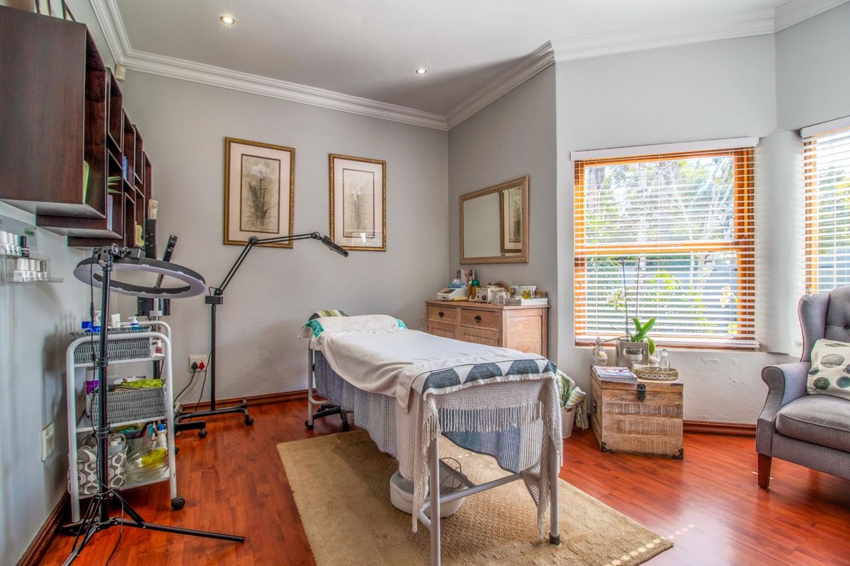 A well-maintained bedroom currently utilized as a treatment room, featuring laminate flooring, crown molding, and natural light through venetian blinds.