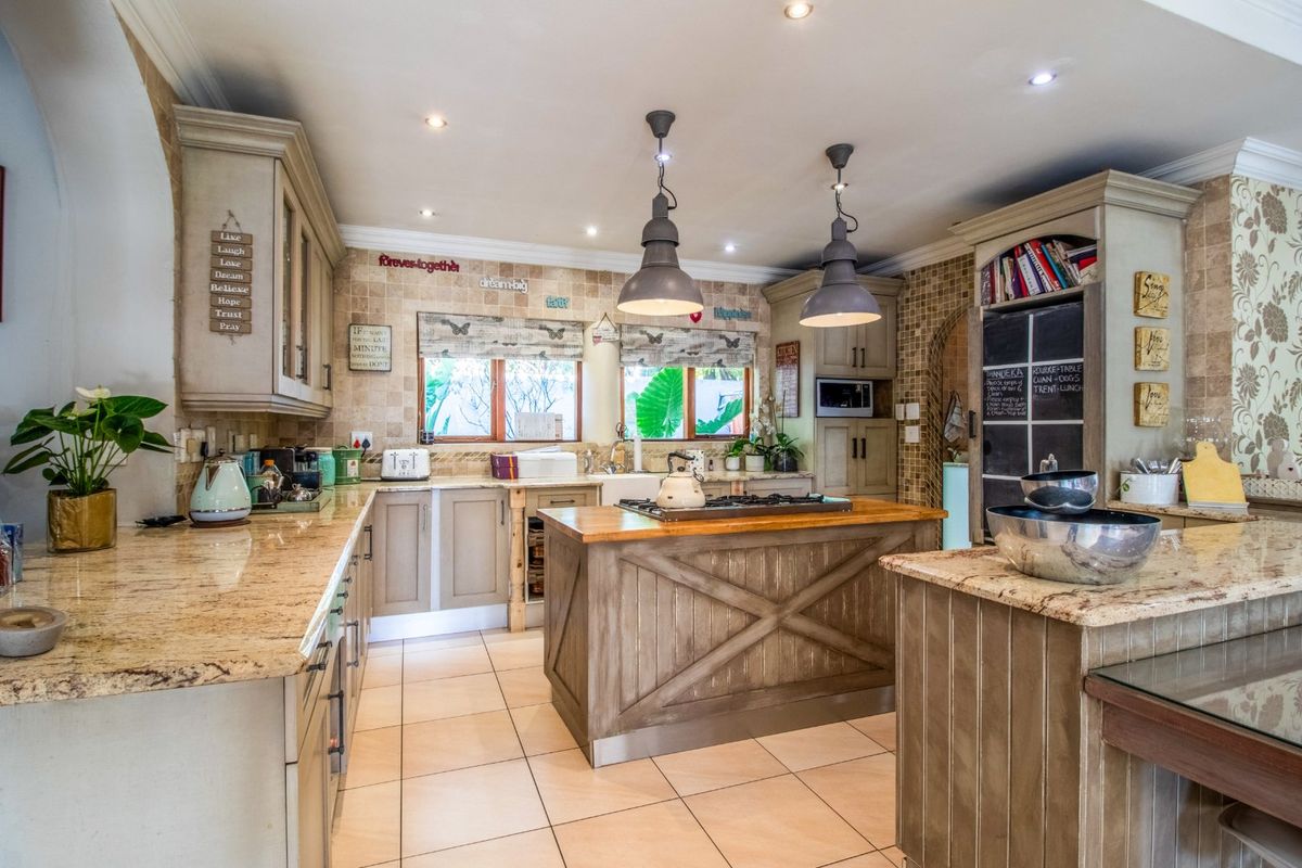 A well-appointed kitchen featuring granite countertops, a central island with a gas hob, custom cabinetry, and stylish pendant lighting.