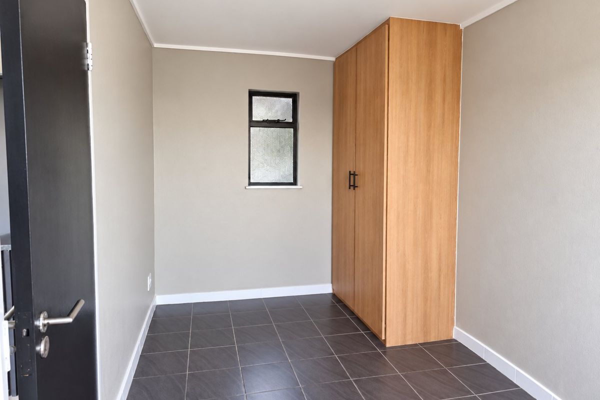 A clean, empty bedroom featuring neutral wall tones, dark tiled flooring, and a built-in wooden wardrobe.