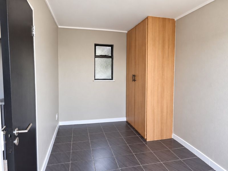 A clean, empty bedroom featuring neutral wall tones, dark tiled flooring, and a built-in wooden wardrobe.