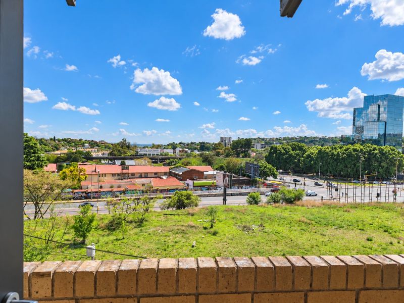 An elevated urban view overlooking a suburban landscape, main roads, and commercial buildings, framed by a brick balcony parapet.