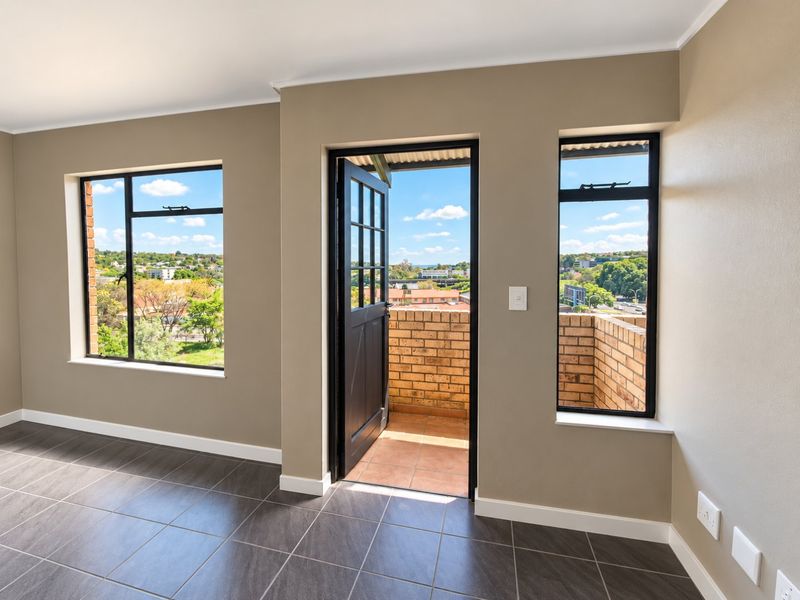 Bright and modern living area featuring dark tiled flooring, large windows, and direct access to a private balcony with scenic views.