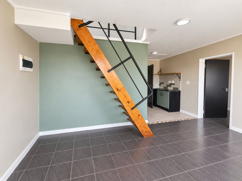 Open plan living area featuring a modern wooden staircase, dark tiled flooring, and a compact kitchen corner with tiled backsplash and cabinetry.