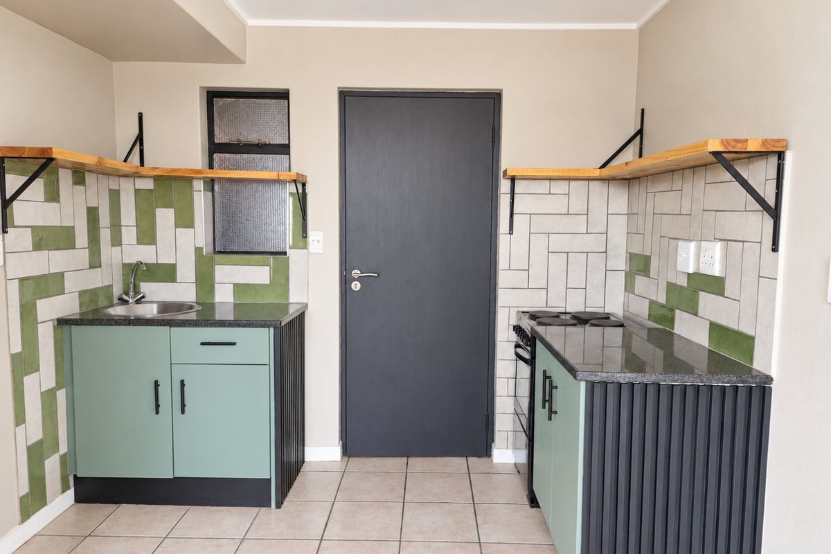Modern kitchen featuring sage green cabinetry, granite countertops, tiled backsplash, floating shelves, and a built-in electric stove.
