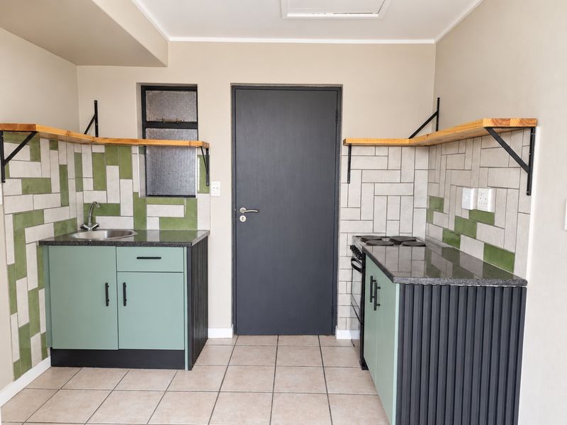 Modern kitchen featuring sage green cabinetry, granite countertops, tiled backsplash, floating shelves, and a built-in electric stove.