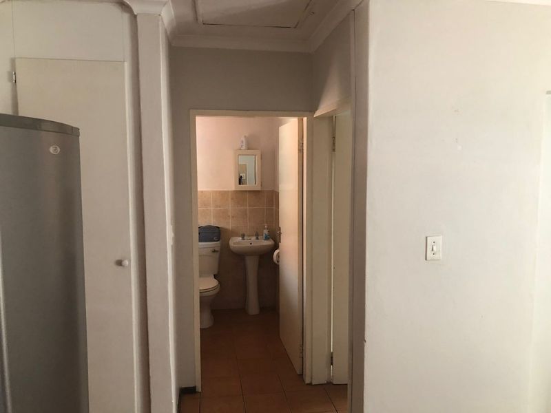 A view from a hallway looking into a small bathroom featuring a pedestal basin and toilet, with adjacent built-in storage cupboards.