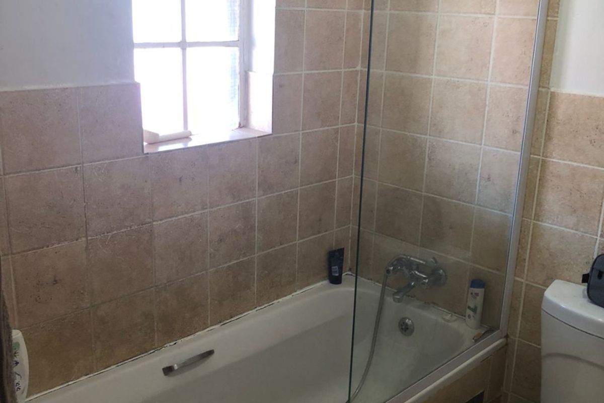 A functional bathroom featuring a bathtub with a glass shower screen, tiled wall finishes, and a standard toilet.