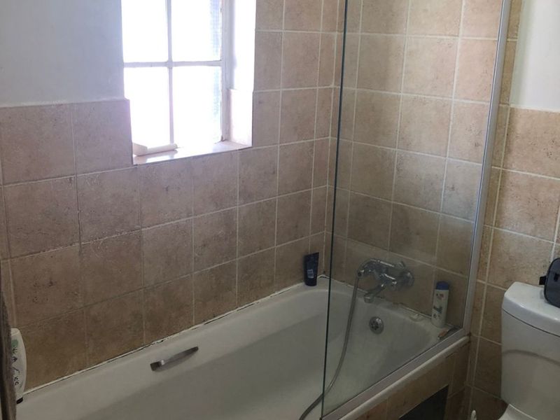 A functional bathroom featuring a bathtub with a glass shower screen, tiled wall finishes, and a standard toilet.