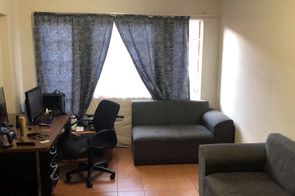 A living room area featuring tiled flooring and a large window, providing a functional space for relaxation or home office use.