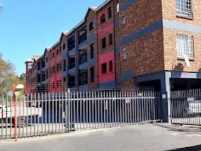 Exterior view of a multi-story apartment complex featuring brick facade, arched windows, and secure gated parking access.