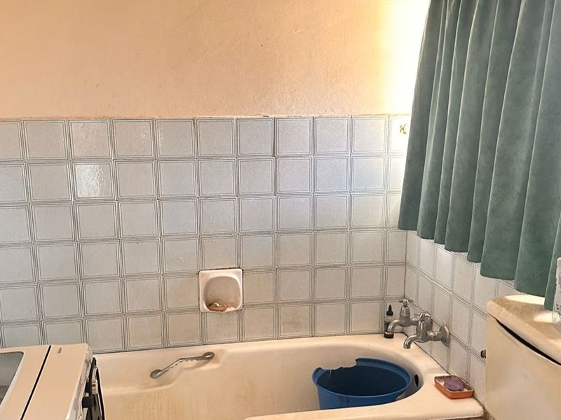 A dated bathroom featuring a built-in bathtub, ceramic tiling, and standard toilet, requiring cosmetic updates and refurbishment to improve its overall condition.
