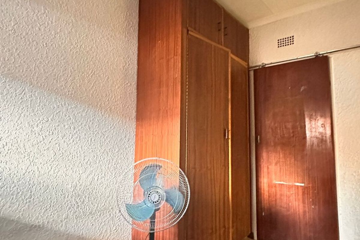 A bedroom featuring a built-in wooden wardrobe, sliding door, and carpeted flooring, offering a blank canvas for renovation or restyling.