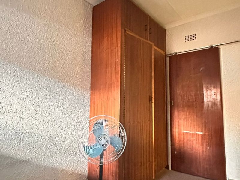 A bedroom featuring a built-in wooden wardrobe, sliding door, and carpeted flooring, offering a blank canvas for renovation or restyling.