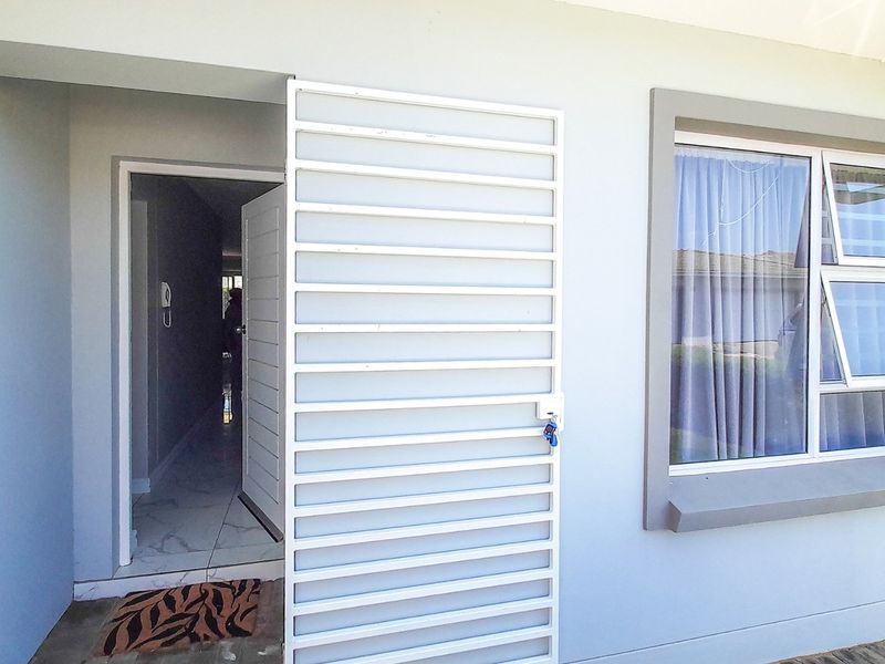 Front entrance of the house featuring a white security gate, aluminium window frame, and tiled flooring at the doorway.
