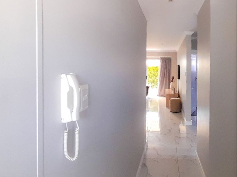 A bright, modern hallway featuring polished marble-look floor tiles, recessed lighting, and a wall-mounted intercom system, leading towards an open living area.