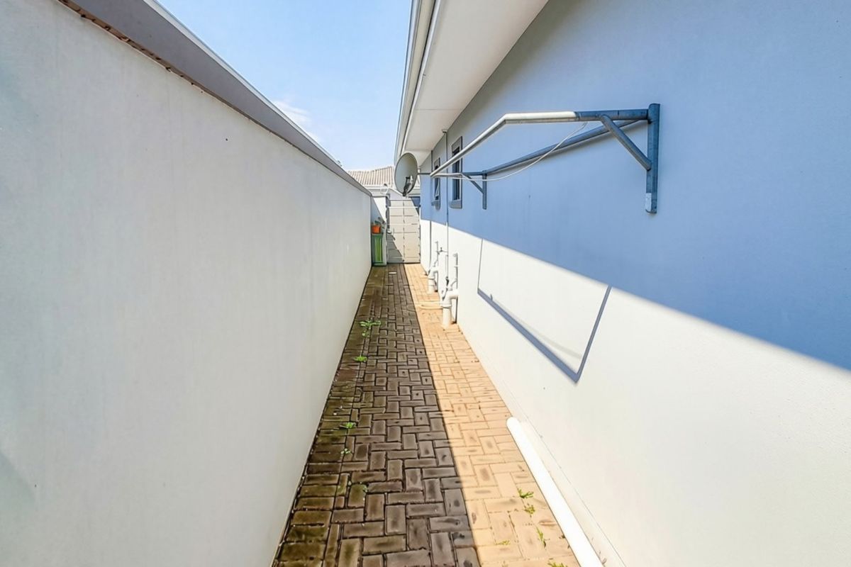 A narrow side passage featuring brick paving, a wall-mounted clothesline, and boundary walling, providing functional utility space along the side of the house.