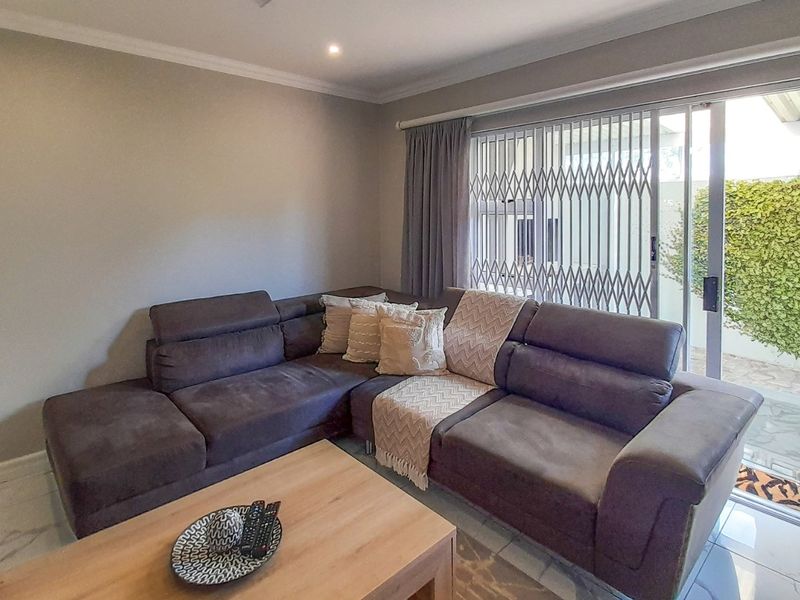 A well-maintained living room featuring tiled flooring, recessed lighting, and a large sliding glass door with a security gate leading to the patio.