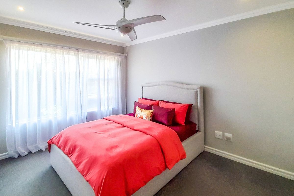 A well-maintained bedroom featuring neutral walls, carpeted flooring, built-in cupboards, and a ceiling fan, offering a comfortable and functional living space.