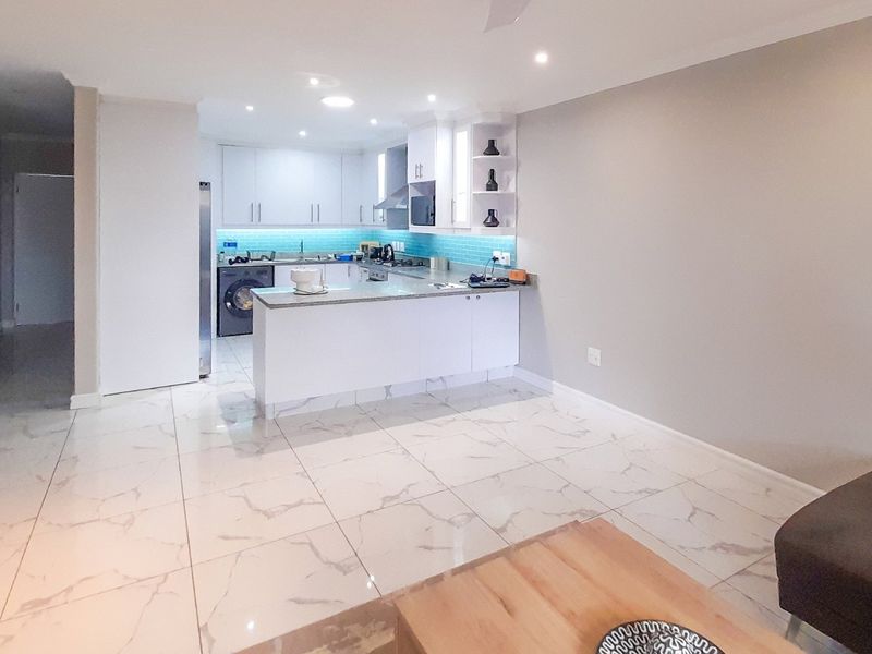 Modern open-plan kitchen featuring sleek white cabinetry, stone countertops, a vibrant tiled backsplash, and high-quality marble-look floor tiles throughout the living space.
