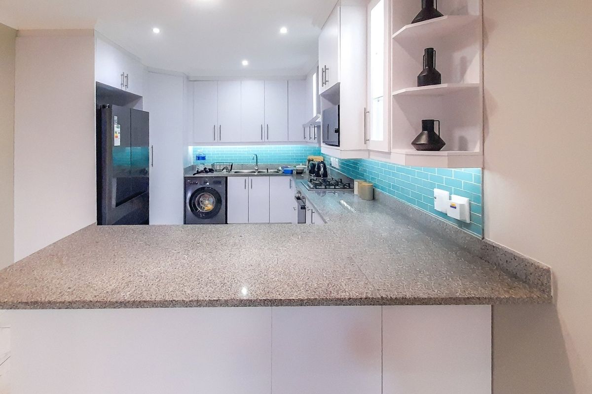 Modern kitchen featuring white cabinetry, granite countertops, a vibrant blue subway tile backsplash, and integrated appliances with recessed lighting.