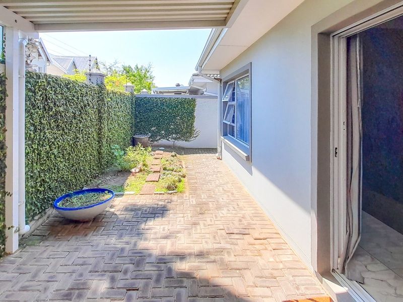 A covered patio area featuring brick paving, a sliding door entrance, and a landscaped boundary wall with climbing greenery.