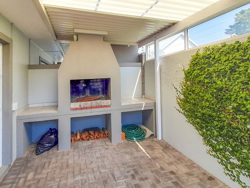 Covered outdoor patio area featuring a built-in braai, paved flooring, and a climbing plant feature wall, ideal for outdoor entertaining.