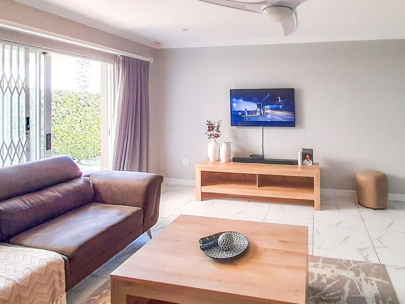 A bright and modern living room featuring large format tiled flooring, a ceiling fan, and a sliding glass door with security gate access to the garden.