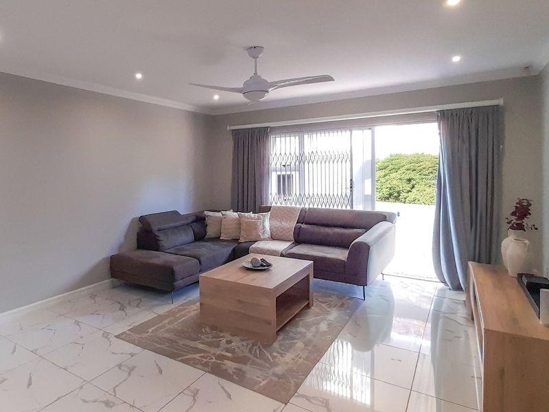 A bright living room featuring polished marble-look floor tiles, recessed downlights, a ceiling fan, and a sliding glass door leading to an outdoor area.