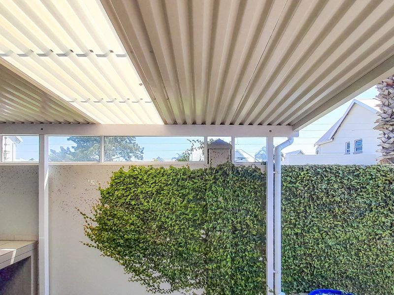 A covered patio area featuring a corrugated metal roof with translucent panels, a built-in braai, and a wall covered in climbing ivy.