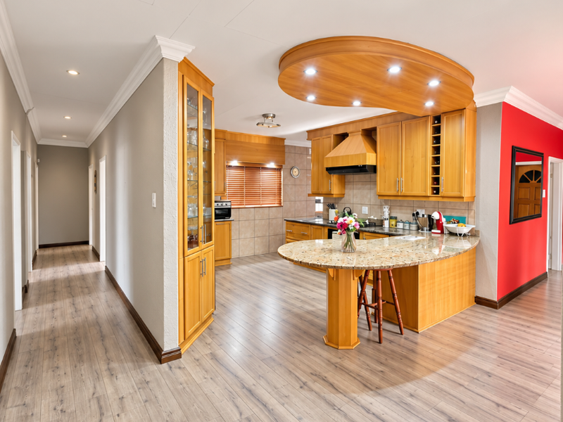 Spacious open-plan kitchen featuring warm wooden cabinetry, granite countertops, and a unique circular ceiling feature with integrated lighting, flowing into a hallway.